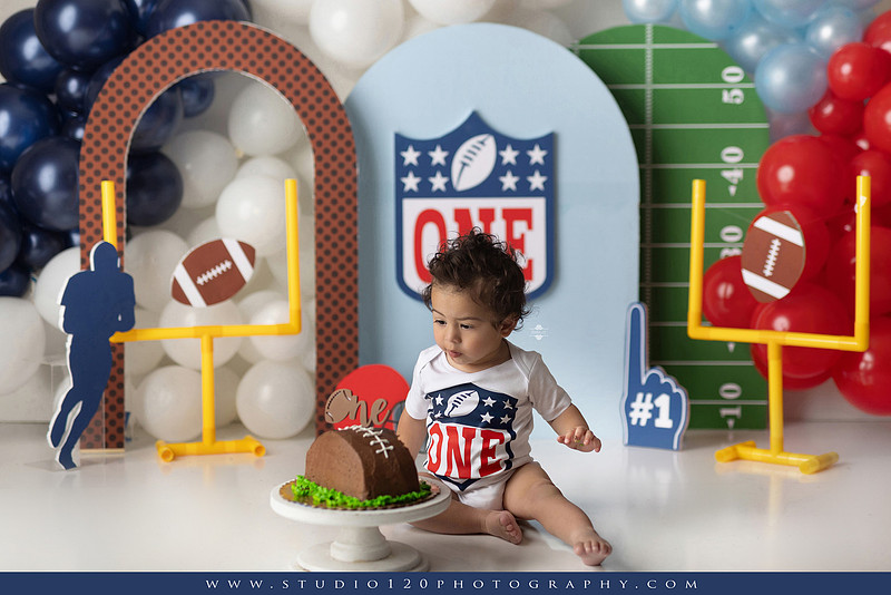 “Studio 120 Photography first birthday football cake smash session featuring a custom football set, milestone portraits, and smash cake celebration.”