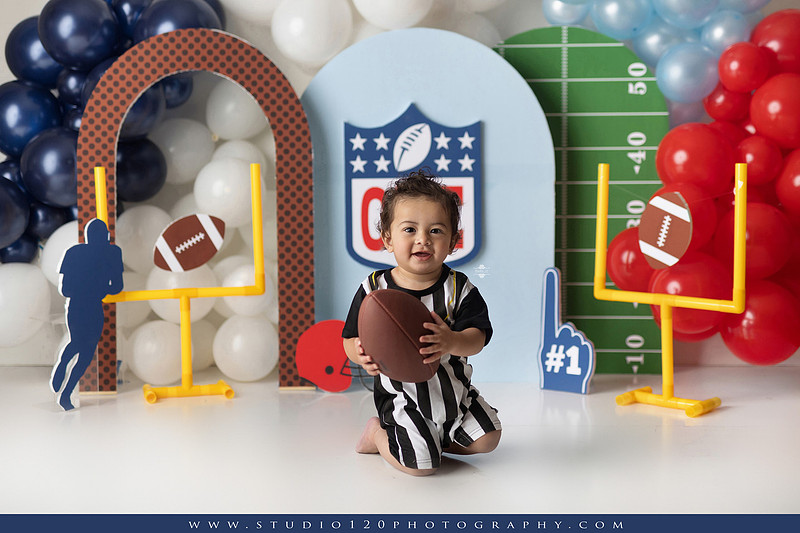 “Studio 120 Photography first birthday football cake smash session featuring a custom football set, milestone portraits, and smash cake celebration.”