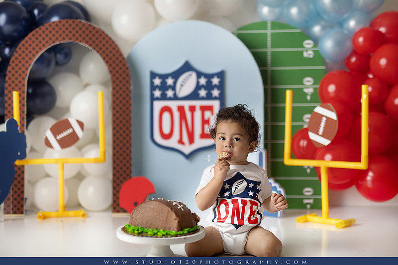 “Studio 120 Photography first birthday football cake smash session featuring a custom football set, milestone portraits, and smash cake celebration.”