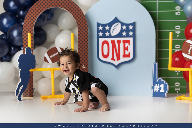 “Studio 120 Photography first birthday football cake smash session featuring a custom football set, milestone portraits, and smash cake celebration.”