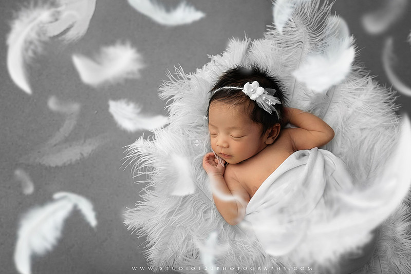 Banksy-inspired newborn photography featuring fine art minimalist styling with angel wings, painted motion effects, and a red heart balloon on a soft gray backdrop