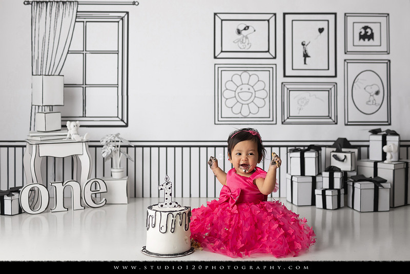 Art-inspired first birthday photo session featuring a toddler in a vibrant pink dress against a graphic black-and-white illustrated set, with visual nods to Takashi Murakami, KAWS, Jeff Koons, and Invader
