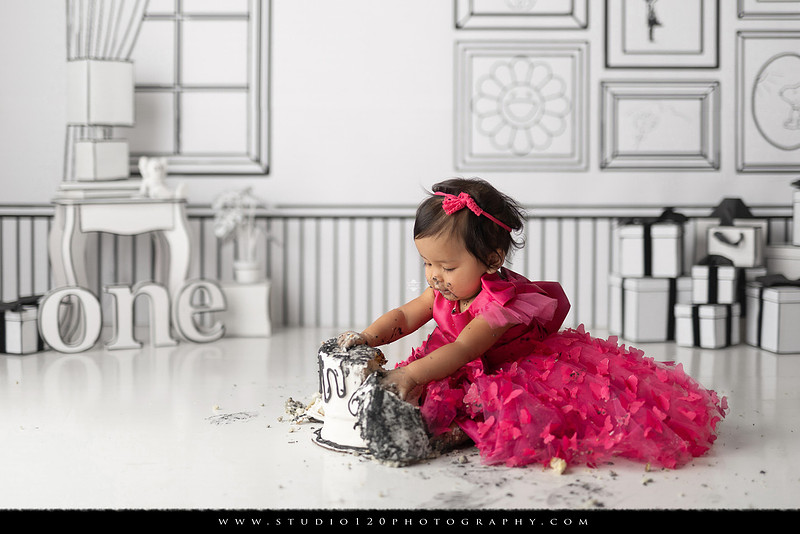 Art-inspired first birthday photo session featuring a toddler in a vibrant pink dress against a graphic black-and-white illustrated set, with visual nods to Takashi Murakami, KAWS, Jeff Koons, and Invader
