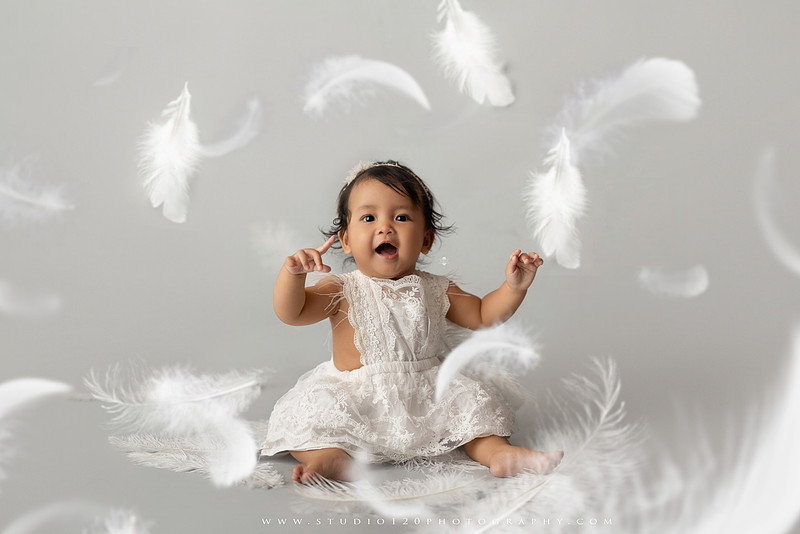 Banksy-inspired newborn photography featuring fine art minimalist styling with angel wings, painted motion effects, and a red heart balloon on a soft gray backdrop