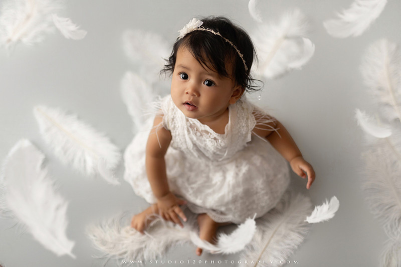 Banksy-inspired newborn photography featuring fine art minimalist styling with angel wings, painted motion effects, and a red heart balloon on a soft gray backdrop