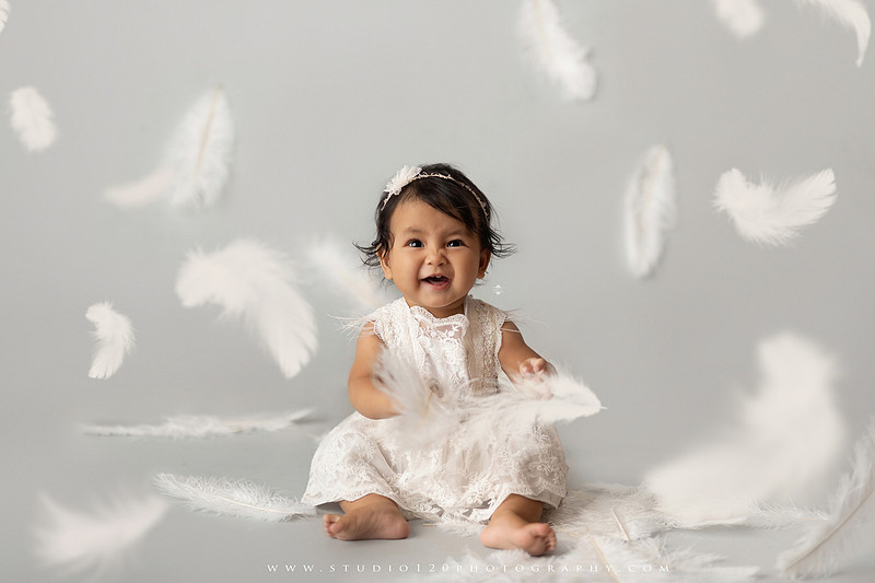 Banksy-inspired newborn photography featuring fine art minimalist styling with angel wings, painted motion effects, and a red heart balloon on a soft gray backdrop
