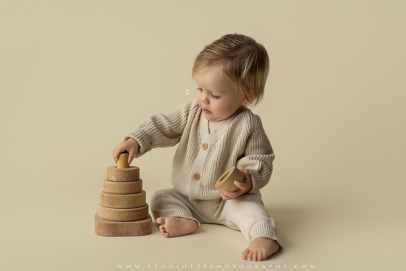 One-year-old baby wearing a cowboy hat sits on a rustic honky-tonk stage with vintage posters, string lights, and a neon “One Night Only” sign during a country-themed milestone photo session.