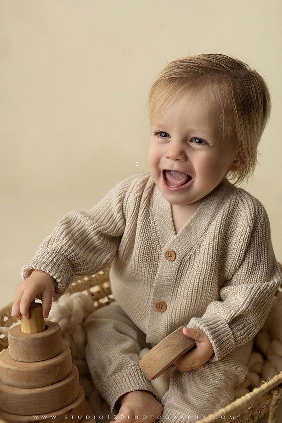 One-year-old baby wearing a cowboy hat sits on a rustic honky-tonk stage with vintage posters, string lights, and a neon “One Night Only” sign during a country-themed milestone photo session.