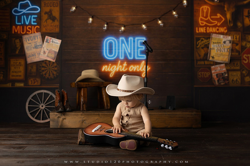 EvotoOne-year-old baby wearing a cowboy hat sits on a rustic honky-tonk stage with vintage posters, string lights, and a neon “One Night Only” sign during a country-themed milestone photo session.