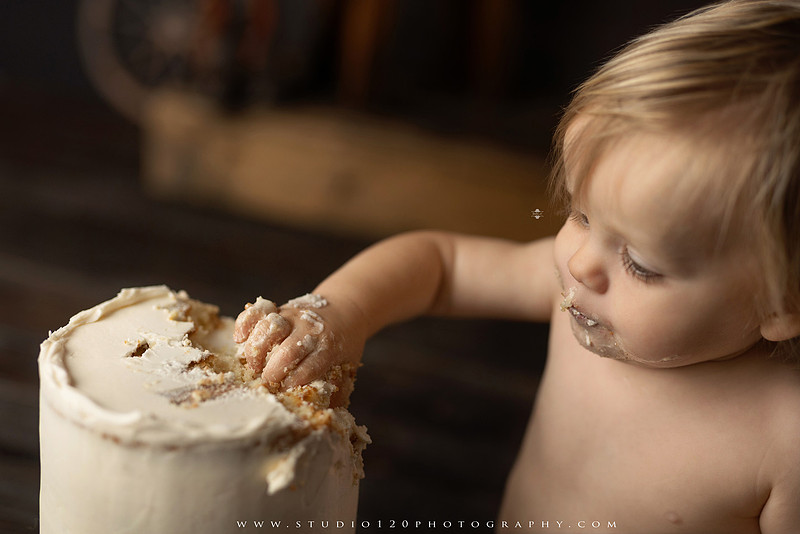 EvotoOne-year-old baby wearing a cowboy hat sits on a rustic honky-tonk stage with vintage posters, string lights, and a neon “One Night Only” sign during a country-themed milestone photo session.