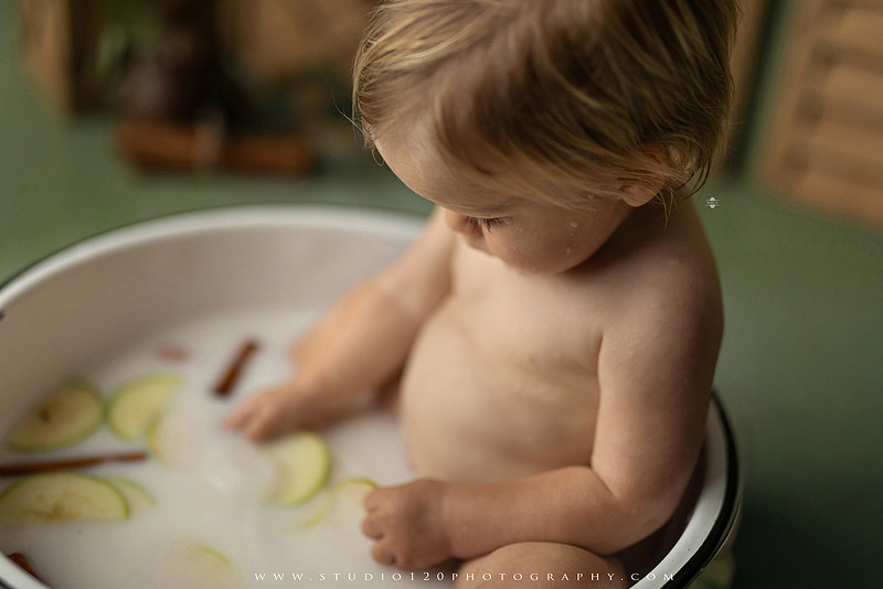 EvotoOne-year-old baby wearing a cowboy hat sits on a rustic honky-tonk stage with vintage posters, string lights, and a neon “One Night Only” sign during a country-themed milestone photo session.