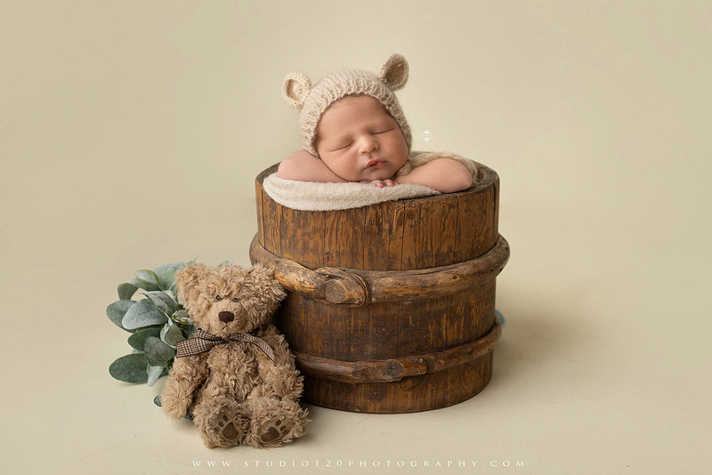 Custom newborn photography session in Ramona, California featuring a baby posed in cozy neutral tones with safari-inspired scenes, teddy bears, and a playful business suit setup, created using studio styling and digital backdrops by a San Diego newborn photographer.