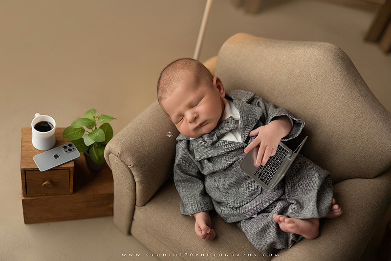 Custom newborn photography session in Ramona, California featuring a baby posed in cozy neutral tones with safari-inspired scenes, teddy bears, and a playful business suit setup, created using studio styling and digital backdrops by a San Diego newborn photographer.