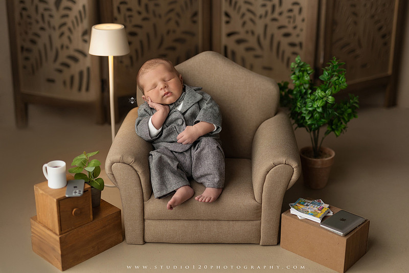 Custom newborn photography session in Ramona, California featuring a baby posed in cozy neutral tones with safari-inspired scenes, teddy bears, and a playful business suit setup, created using studio styling and digital backdrops by a San Diego newborn photographer.