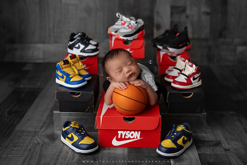 “basketball themed newborn photo with baby holding mini basketball and Nike sneakers backdrop”
“sports newborn photography basketball style with sneaker stack and baby portrait”
“adorable infant with basketball and stacked shoes Nike brand inspired sports session”