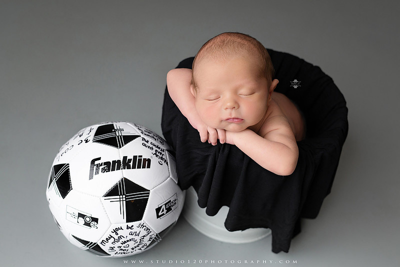 “newborn baby soccer themed photo holding black and white soccer ball”
“soccer sports newborn portrait with baby curled around soccer ball”
“infant soccer photography session with classic soccer ball and soft wrap”