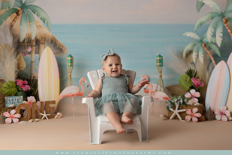 “first birthday portrait of baby in white dress with floral accents in light and airy studio”
“elegant first birthday portrait session with baby in white dress and neutral backdrop”
“luxe coastal cake smash with beach themed backdrop, flamingos and tropical decor”
“baby girl beach themed cake smash with pastel cake and tropical surfboard props”
“coastal first birthday cake smash with flamingo accents and soft beach colors”
“tropical cake smash photography featuring baby and pastel beach themed set”
“baby enjoying cake smash in coastal themed studio with palm trees and flamingos”
“beach inspired cake smash session with baby standing in cake and tropical decor”
“luxury cake smash photography with coastal beach theme and soft pastel tones”