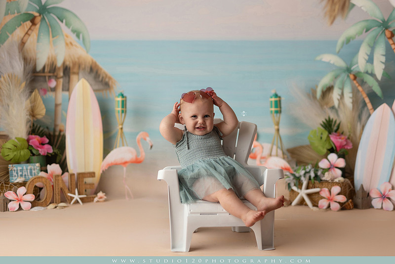 “first birthday portrait of baby in white dress with floral accents in light and airy studio”
“elegant first birthday portrait session with baby in white dress and neutral backdrop”
“luxe coastal cake smash with beach themed backdrop, flamingos and tropical decor”
“baby girl beach themed cake smash with pastel cake and tropical surfboard props”
“coastal first birthday cake smash with flamingo accents and soft beach colors”
“tropical cake smash photography featuring baby and pastel beach themed set”
“baby enjoying cake smash in coastal themed studio with palm trees and flamingos”
“beach inspired cake smash session with baby standing in cake and tropical decor”
“luxury cake smash photography with coastal beach theme and soft pastel tones”