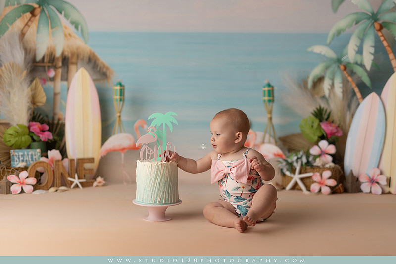 “first birthday portrait of baby in white dress with floral accents in light and airy studio”
“elegant first birthday portrait session with baby in white dress and neutral backdrop”
“luxe coastal cake smash with beach themed backdrop, flamingos and tropical decor”
“baby girl beach themed cake smash with pastel cake and tropical surfboard props”
“coastal first birthday cake smash with flamingo accents and soft beach colors”
“tropical cake smash photography featuring baby and pastel beach themed set”
“baby enjoying cake smash in coastal themed studio with palm trees and flamingos”
“beach inspired cake smash session with baby standing in cake and tropical decor”
“luxury cake smash photography with coastal beach theme and soft pastel tones”