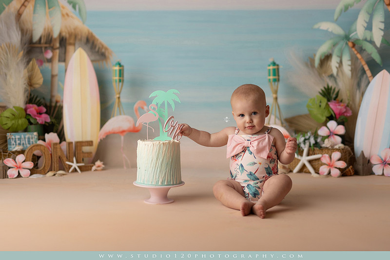 “first birthday portrait of baby in white dress with floral accents in light and airy studio”
“elegant first birthday portrait session with baby in white dress and neutral backdrop”
“luxe coastal cake smash with beach themed backdrop, flamingos and tropical decor”
“baby girl beach themed cake smash with pastel cake and tropical surfboard props”
“coastal first birthday cake smash with flamingo accents and soft beach colors”
“tropical cake smash photography featuring baby and pastel beach themed set”
“baby enjoying cake smash in coastal themed studio with palm trees and flamingos”
“beach inspired cake smash session with baby standing in cake and tropical decor”
“luxury cake smash photography with coastal beach theme and soft pastel tones”