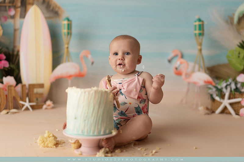 “first birthday portrait of baby in white dress with floral accents in light and airy studio”
“elegant first birthday portrait session with baby in white dress and neutral backdrop”
“luxe coastal cake smash with beach themed backdrop, flamingos and tropical decor”
“baby girl beach themed cake smash with pastel cake and tropical surfboard props”
“coastal first birthday cake smash with flamingo accents and soft beach colors”
“tropical cake smash photography featuring baby and pastel beach themed set”
“baby enjoying cake smash in coastal themed studio with palm trees and flamingos”
“beach inspired cake smash session with baby standing in cake and tropical decor”
“luxury cake smash photography with coastal beach theme and soft pastel tones”