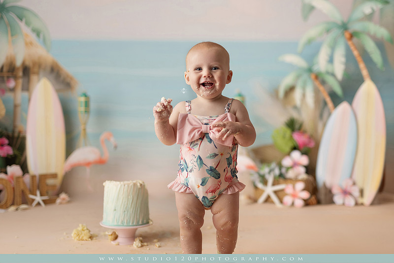 “first birthday portrait of baby in white dress with floral accents in light and airy studio”
“elegant first birthday portrait session with baby in white dress and neutral backdrop”
“luxe coastal cake smash with beach themed backdrop, flamingos and tropical decor”
“baby girl beach themed cake smash with pastel cake and tropical surfboard props”
“coastal first birthday cake smash with flamingo accents and soft beach colors”
“tropical cake smash photography featuring baby and pastel beach themed set”
“baby enjoying cake smash in coastal themed studio with palm trees and flamingos”
“beach inspired cake smash session with baby standing in cake and tropical decor”
“luxury cake smash photography with coastal beach theme and soft pastel tones”