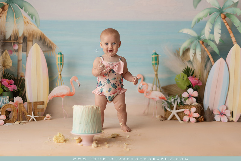 “first birthday portrait of baby in white dress with floral accents in light and airy studio”
“elegant first birthday portrait session with baby in white dress and neutral backdrop”
“luxe coastal cake smash with beach themed backdrop, flamingos and tropical decor”
“baby girl beach themed cake smash with pastel cake and tropical surfboard props”
“coastal first birthday cake smash with flamingo accents and soft beach colors”
“tropical cake smash photography featuring baby and pastel beach themed set”
“baby enjoying cake smash in coastal themed studio with palm trees and flamingos”
“beach inspired cake smash session with baby standing in cake and tropical decor”
“luxury cake smash photography with coastal beach theme and soft pastel tones”