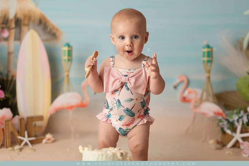 “first birthday portrait of baby in white dress with floral accents in light and airy studio”
“elegant first birthday portrait session with baby in white dress and neutral backdrop”
“luxe coastal cake smash with beach themed backdrop, flamingos and tropical decor”
“baby girl beach themed cake smash with pastel cake and tropical surfboard props”
“coastal first birthday cake smash with flamingo accents and soft beach colors”
“tropical cake smash photography featuring baby and pastel beach themed set”
“baby enjoying cake smash in coastal themed studio with palm trees and flamingos”
“beach inspired cake smash session with baby standing in cake and tropical decor”
“luxury cake smash photography with coastal beach theme and soft pastel tones”