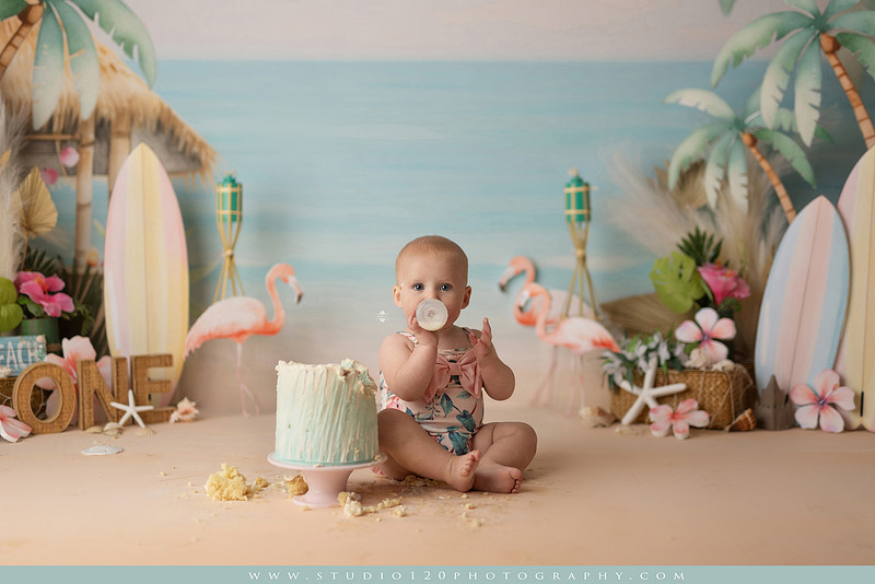“first birthday portrait of baby in white dress with floral accents in light and airy studio”
“elegant first birthday portrait session with baby in white dress and neutral backdrop”
“luxe coastal cake smash with beach themed backdrop, flamingos and tropical decor”
“baby girl beach themed cake smash with pastel cake and tropical surfboard props”
“coastal first birthday cake smash with flamingo accents and soft beach colors”
“tropical cake smash photography featuring baby and pastel beach themed set”
“baby enjoying cake smash in coastal themed studio with palm trees and flamingos”
“beach inspired cake smash session with baby standing in cake and tropical decor”
“luxury cake smash photography with coastal beach theme and soft pastel tones”