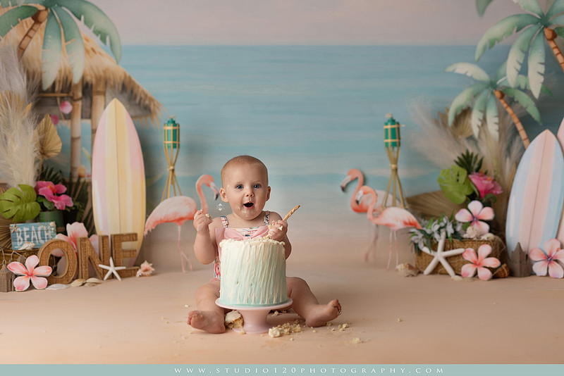 “first birthday portrait of baby in white dress with floral accents in light and airy studio”
“elegant first birthday portrait session with baby in white dress and neutral backdrop”
“luxe coastal cake smash with beach themed backdrop, flamingos and tropical decor”
“baby girl beach themed cake smash with pastel cake and tropical surfboard props”
“coastal first birthday cake smash with flamingo accents and soft beach colors”
“tropical cake smash photography featuring baby and pastel beach themed set”
“baby enjoying cake smash in coastal themed studio with palm trees and flamingos”
“beach inspired cake smash session with baby standing in cake and tropical decor”
“luxury cake smash photography with coastal beach theme and soft pastel tones”