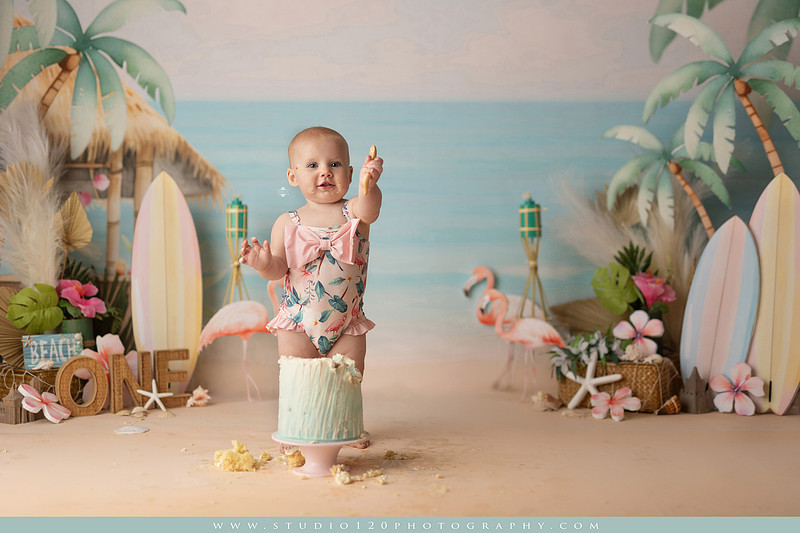 “first birthday portrait of baby in white dress with floral accents in light and airy studio”
“elegant first birthday portrait session with baby in white dress and neutral backdrop”
“luxe coastal cake smash with beach themed backdrop, flamingos and tropical decor”
“baby girl beach themed cake smash with pastel cake and tropical surfboard props”
“coastal first birthday cake smash with flamingo accents and soft beach colors”
“tropical cake smash photography featuring baby and pastel beach themed set”
“baby enjoying cake smash in coastal themed studio with palm trees and flamingos”
“beach inspired cake smash session with baby standing in cake and tropical decor”
“luxury cake smash photography with coastal beach theme and soft pastel tones”