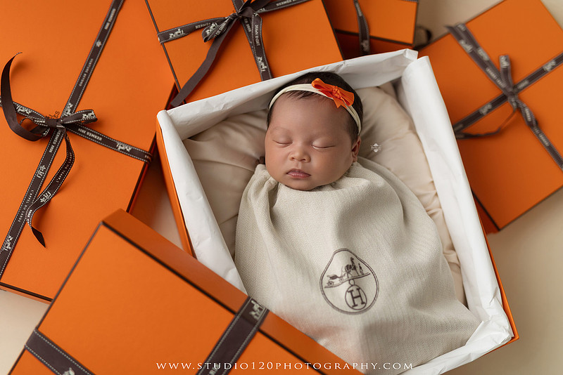 Hermès inspired newborn photography featuring baby girl posed in luxury orange gift box setup at Studio 120 Photography in San Diego County.