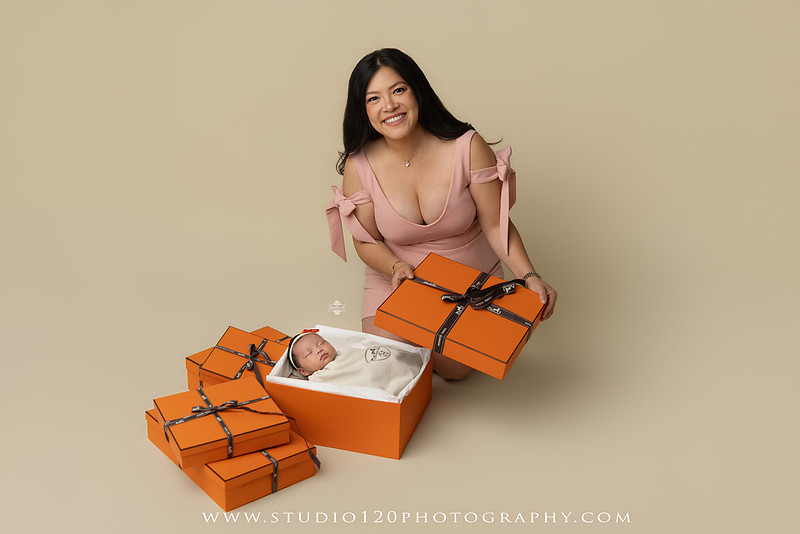 Hermès inspired newborn photography featuring baby girl posed in luxury orange gift box setup at Studio 120 Photography in San Diego County.