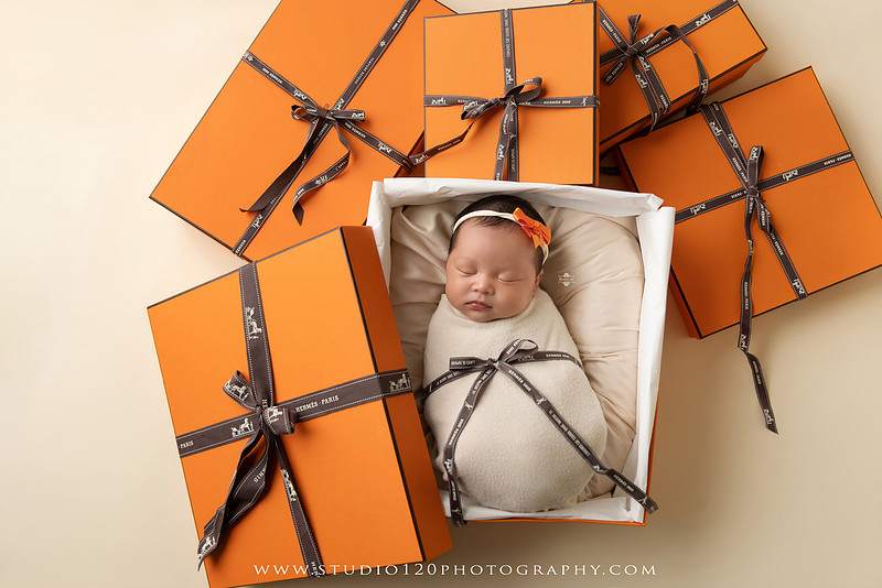 Hermès inspired newborn photography featuring baby girl posed in luxury orange gift box setup at Studio 120 Photography in San Diego County.