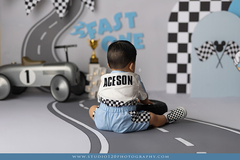 Fast One Mickey Mouse race car cake smash featuring custom race track backdrop, checkered flags, vintage race car prop, and first birthday cake in San Diego