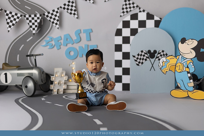 Fast One Mickey Mouse race car cake smash featuring custom race track backdrop, checkered flags, vintage race car prop, and first birthday cake in San Diego