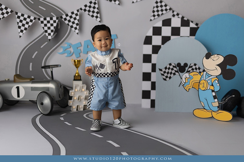 Fast One Mickey Mouse race car cake smash featuring custom race track backdrop, checkered flags, vintage race car prop, and first birthday cake in San Diego