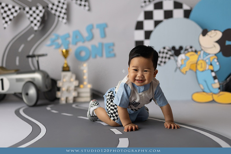 Fast One Mickey Mouse race car cake smash featuring custom race track backdrop, checkered flags, vintage race car prop, and first birthday cake in San Diego