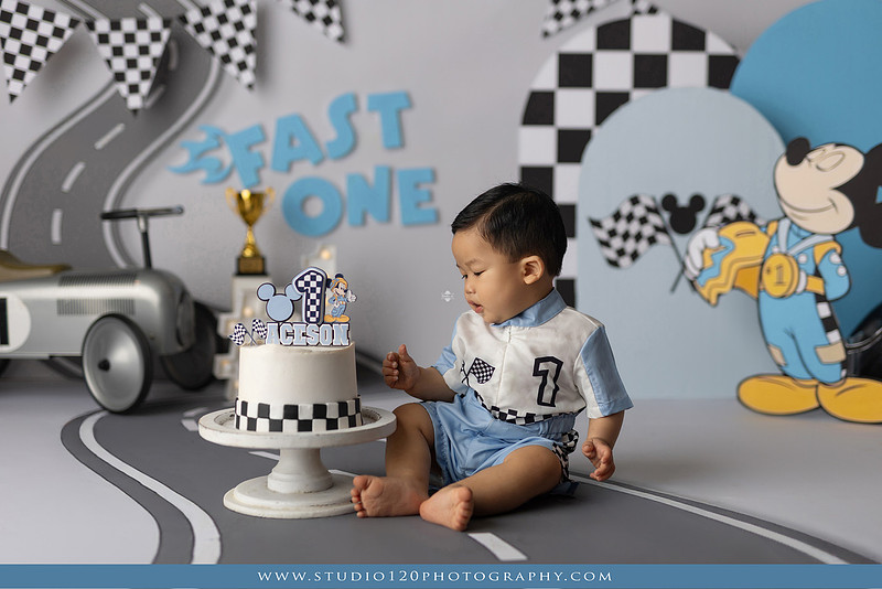 Fast One Mickey Mouse race car cake smash featuring custom race track backdrop, checkered flags, vintage race car prop, and first birthday cake in San Diego
