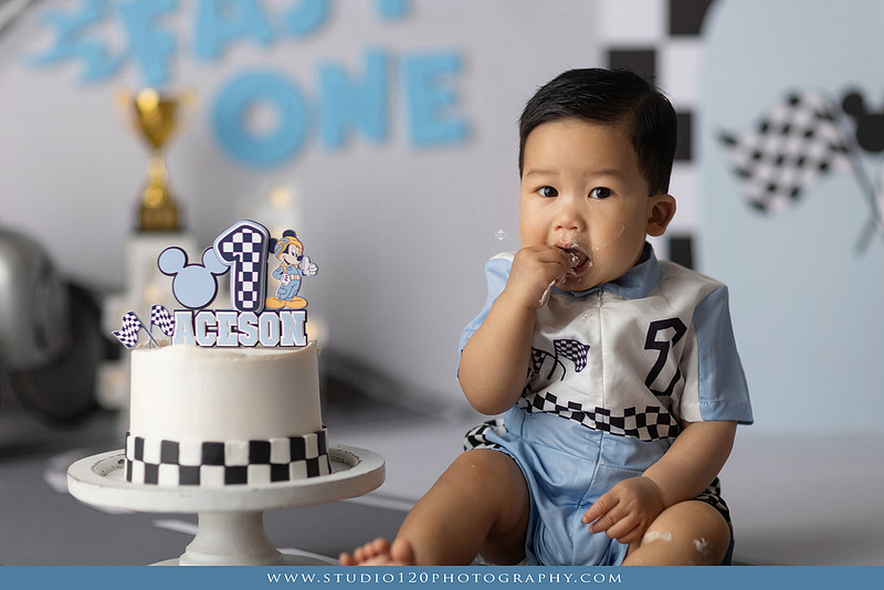 Fast One Mickey Mouse race car cake smash featuring custom race track backdrop, checkered flags, vintage race car prop, and first birthday cake in San Diego