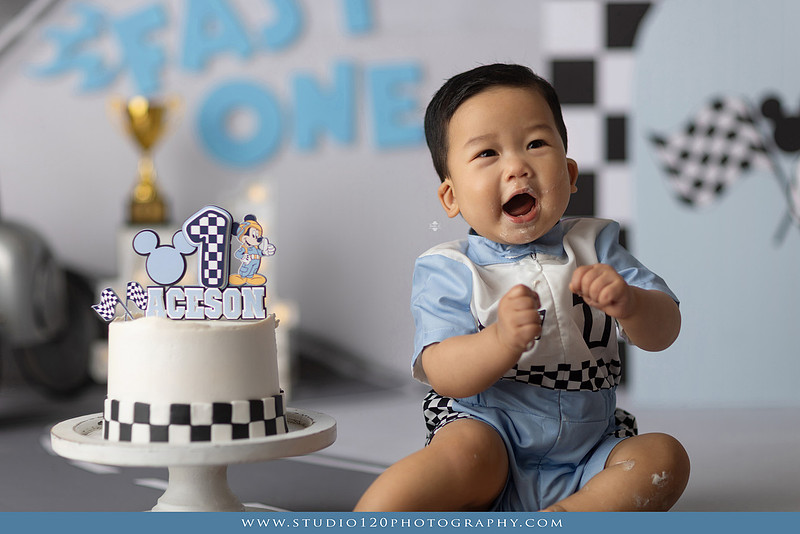 Fast One Mickey Mouse race car cake smash featuring custom race track backdrop, checkered flags, vintage race car prop, and first birthday cake in San Diego
