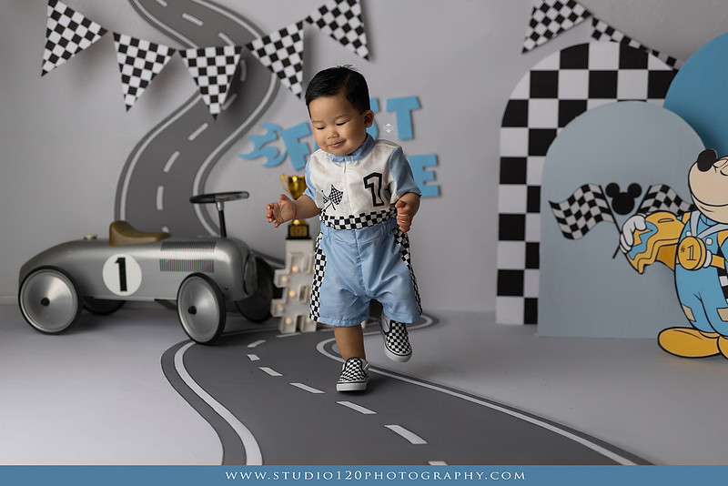 Fast One Mickey Mouse race car cake smash featuring custom race track backdrop, checkered flags, vintage race car prop, and first birthday cake in San Diego