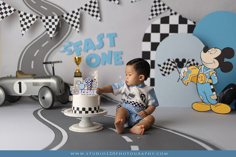 Fast One Mickey Mouse race car cake smash featuring custom race track backdrop, checkered flags, vintage race car prop, and first birthday cake in San Diego