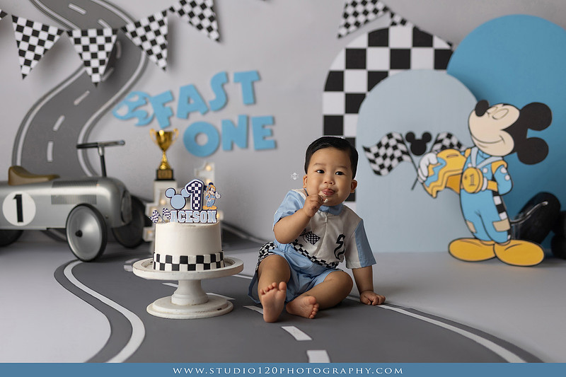 Fast One Mickey Mouse race car cake smash featuring custom race track backdrop, checkered flags, vintage race car prop, and first birthday cake in San Diego