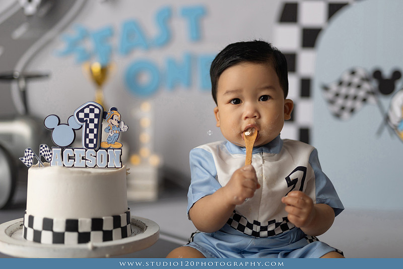 Fast One Mickey Mouse race car cake smash featuring custom race track backdrop, checkered flags, vintage race car prop, and first birthday cake in San Diego