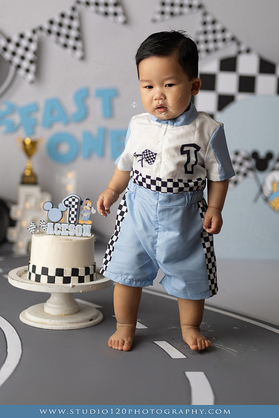 Fast One Mickey Mouse race car cake smash featuring custom race track backdrop, checkered flags, vintage race car prop, and first birthday cake in San Diego