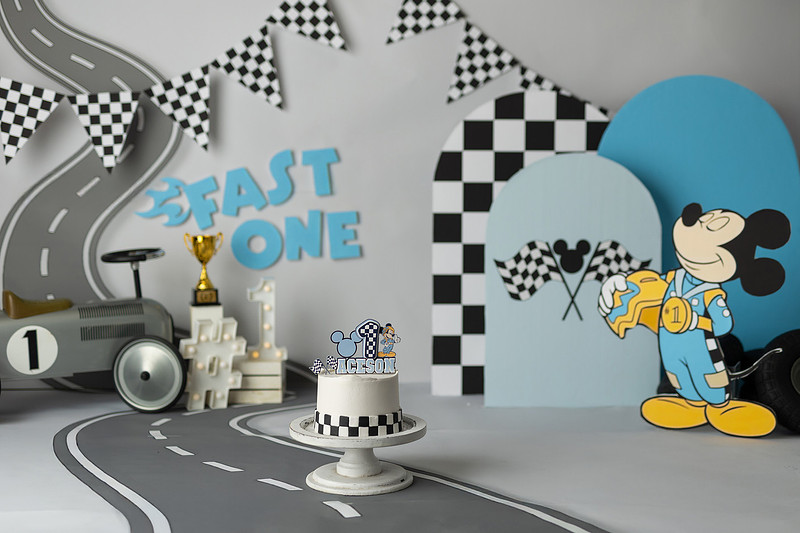 Fast One Mickey Mouse race car cake smash featuring custom race track backdrop, checkered flags, vintage race car prop, and first birthday cake in San Diego
