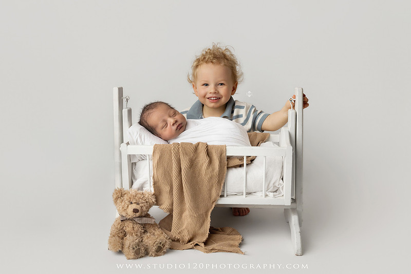 Big brother smiling beside his newborn baby brother during a sibling newborn photography session.