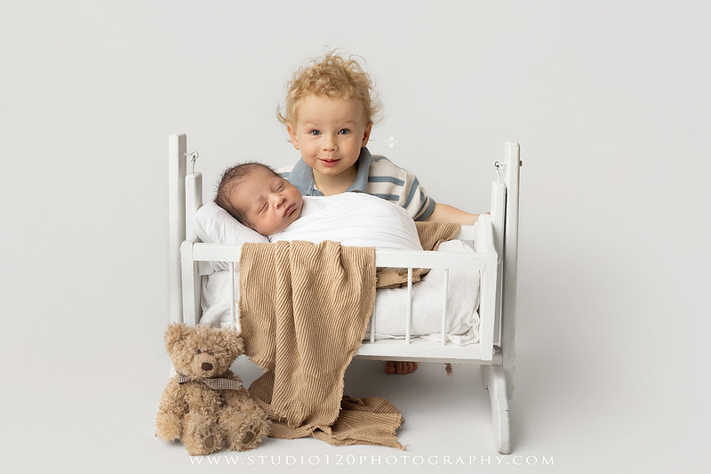 Big brother smiling beside his newborn baby brother during a sibling newborn photography session.