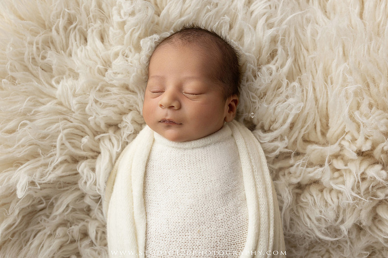 Big brother smiling beside his newborn baby brother during a sibling newborn photography session.